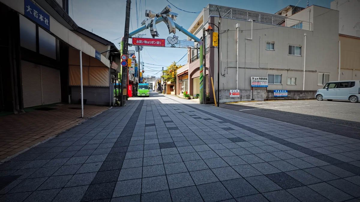 七尾 リボン通り 商店街入口 「リボン通り」と書かれたアーチが架かる商店街入口。左に「大若本社」の建物と閉まったシャッター。奥に緑のバスが見える