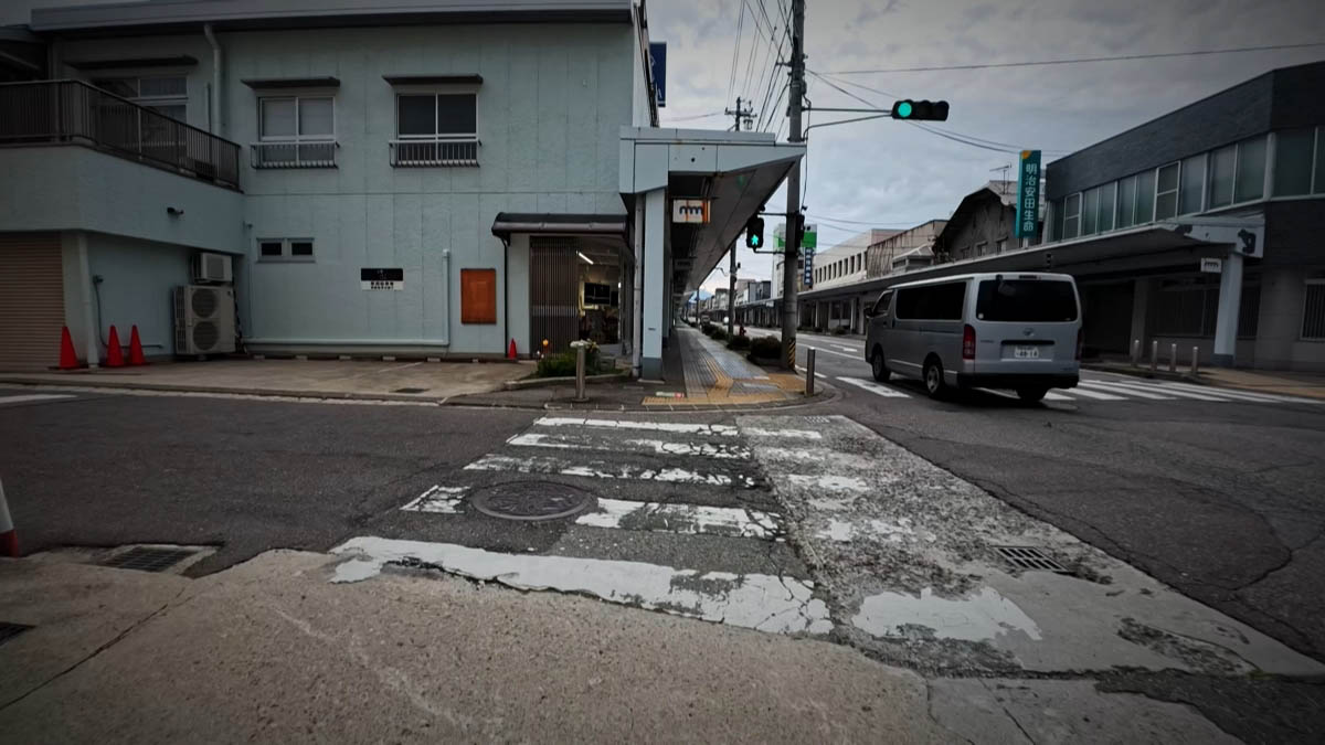 信濃大町駅近くの交差点 横断歩道の向こうにアーケードの入口が見える交差点。右に明治安田生命の看板