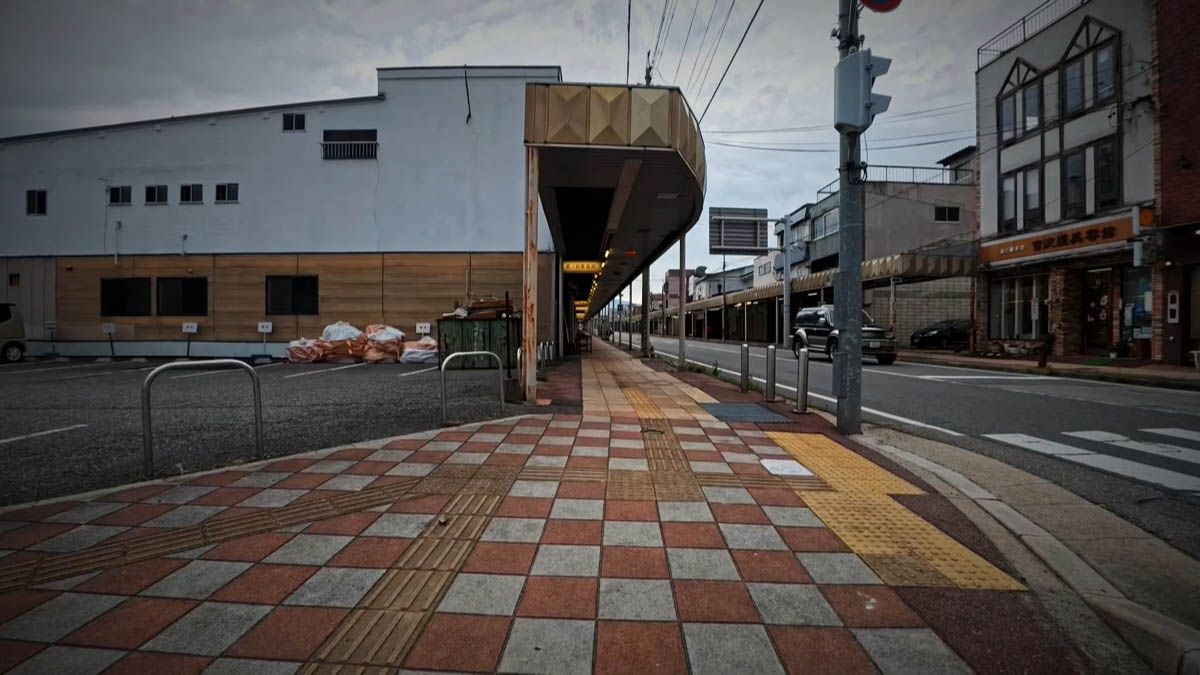 アーケード沿いの歩道 市松模様の歩道と点字ブロック。左手にアーケード、右手に吉沢美容院の看板