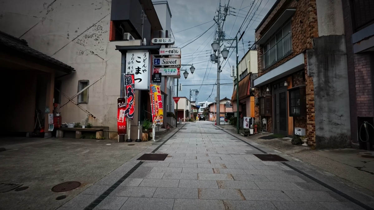 うどんや こまつ付近 うどんや こまつの看板と赤いのぼり。石畳の通りの奥にスナックや料理店の看板