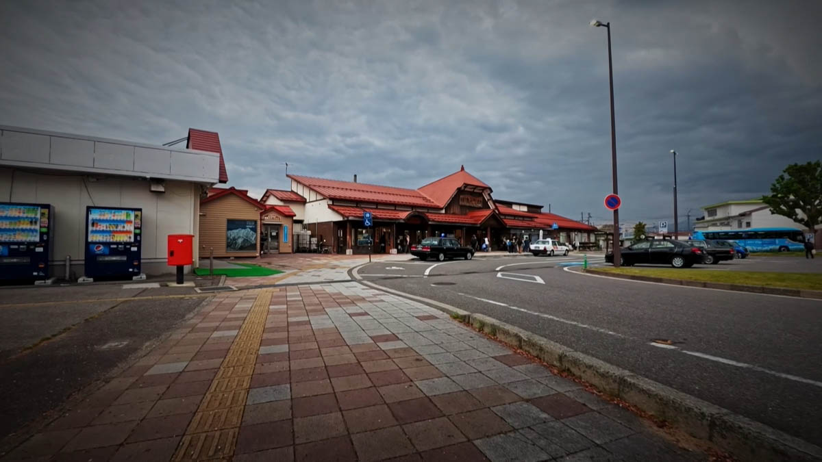信濃大町駅 駅前広場 信濃大町駅の駅前広場。赤茶色の屋根の駅舎とタクシー、点字ブロックの敷かれた広場