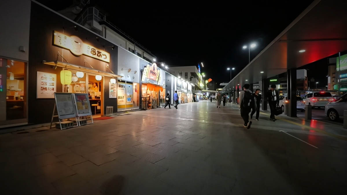 A kushi-katsu shop and Katsumon near the station, with car lights beyond a covered walkway