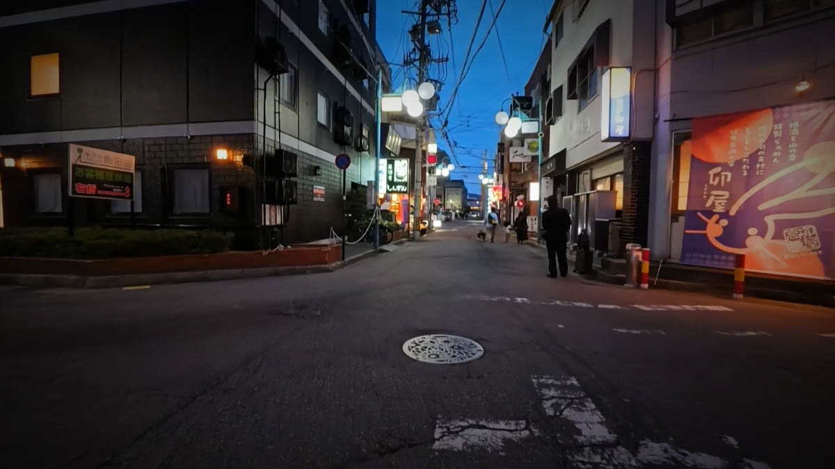A narrow street with a noren for Uya, a shop selling local sake and mountain food, and a round white streetlamp
