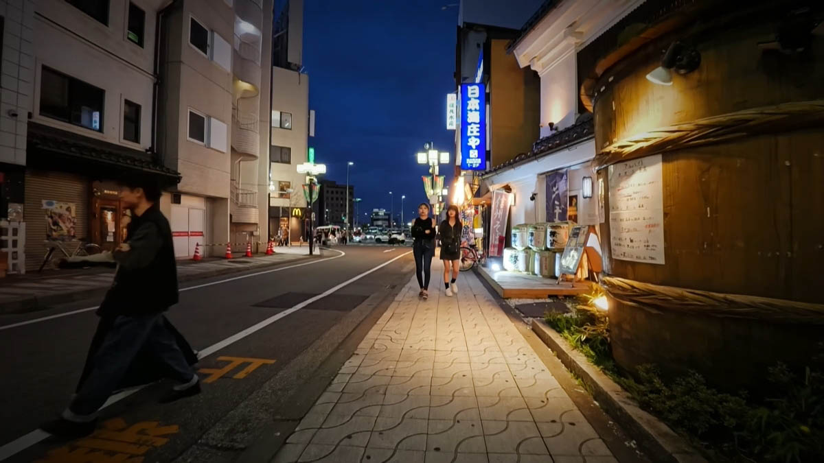 A vertical Shinshu soba sign and sake barrels; a blue Nihonkai Shoya sign further down