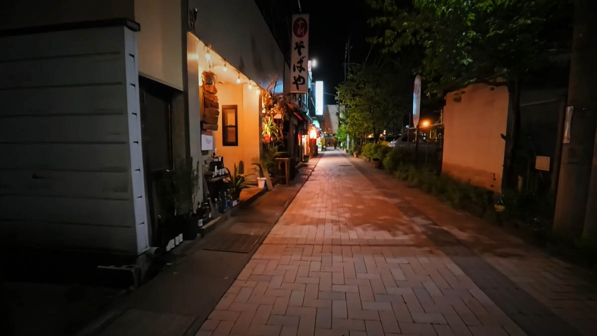 十割そばや 細い通り。十割そばやの縦看板と電球、奥に青い看板