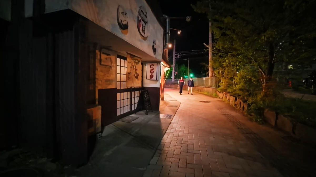だるま だるまの看板がある店先。だるまの絵と格子戸、奥へ歩く人