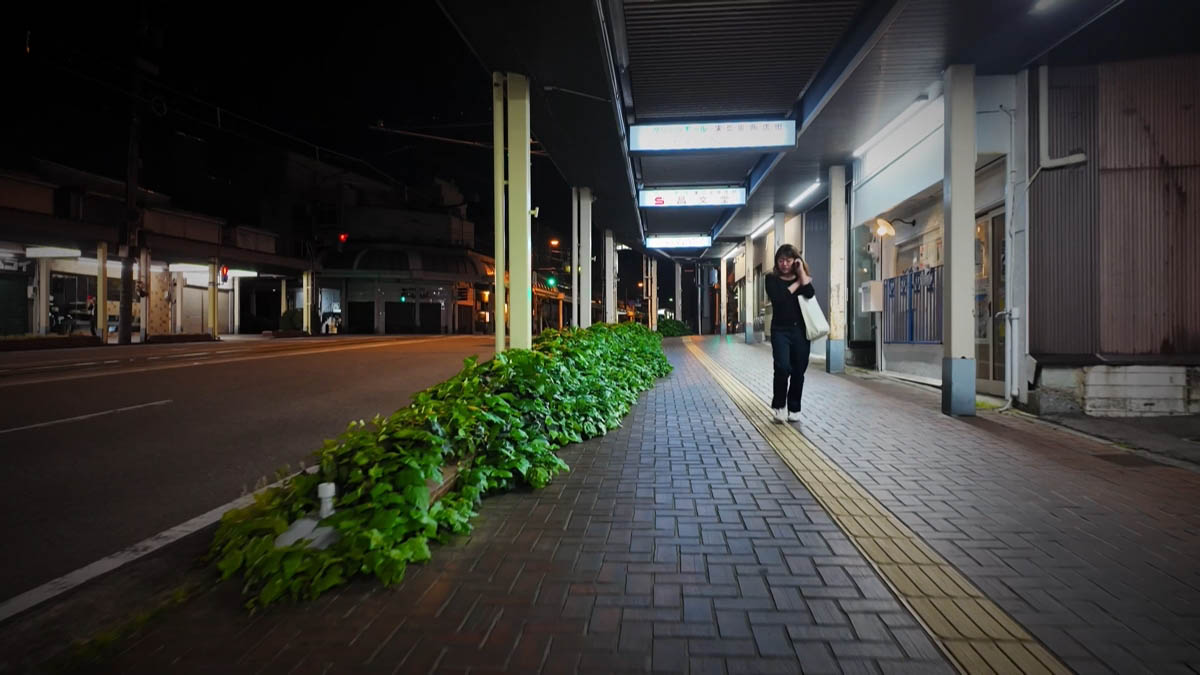 Shobundo Shobundo signs along a covered walkway; hedge on the left, woman walking on the right