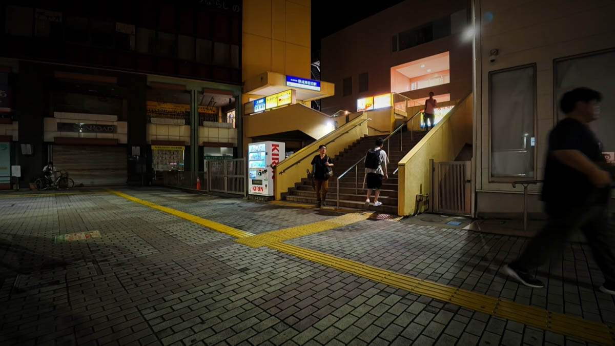 Keisei Tsudanuma Station Stairs at Keisei Tsudanuma Station entrance; blue station sign, KIRIN vending machine, and SUNROAD shutter