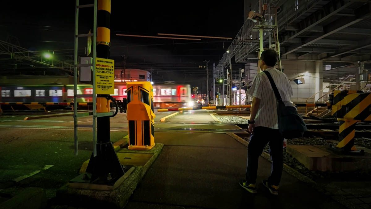 Railroad crossing Person waiting at a railroad crossing as a blurred train passes; lowered gates and yellow emergency sign