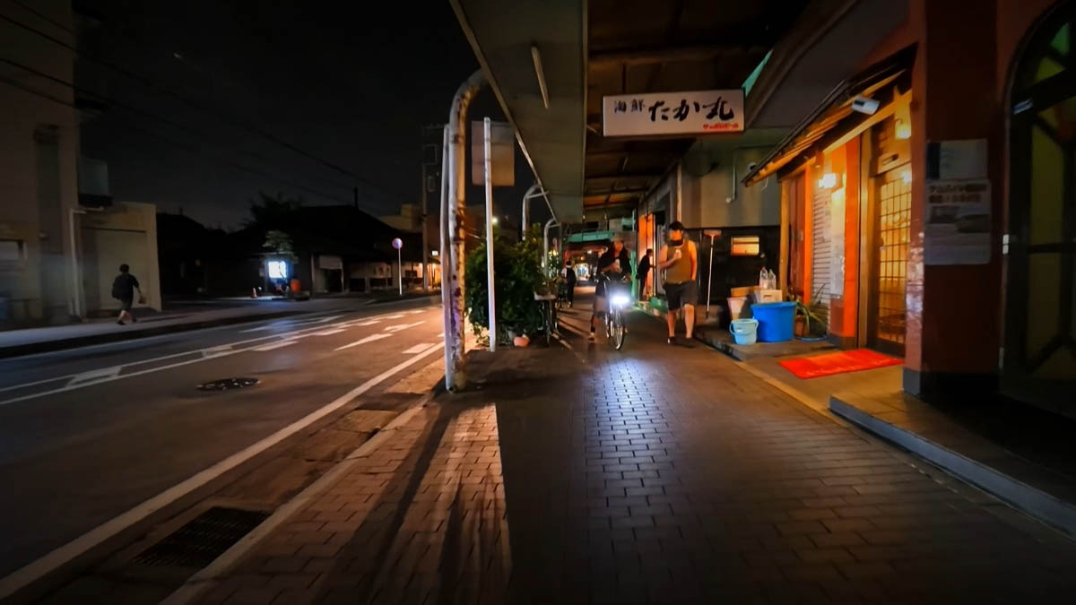 Kaisen Takamaru Kaisen Takamaru seafood shop with a white sign and warm orange interior; a bicycle approaches on the sidewalk