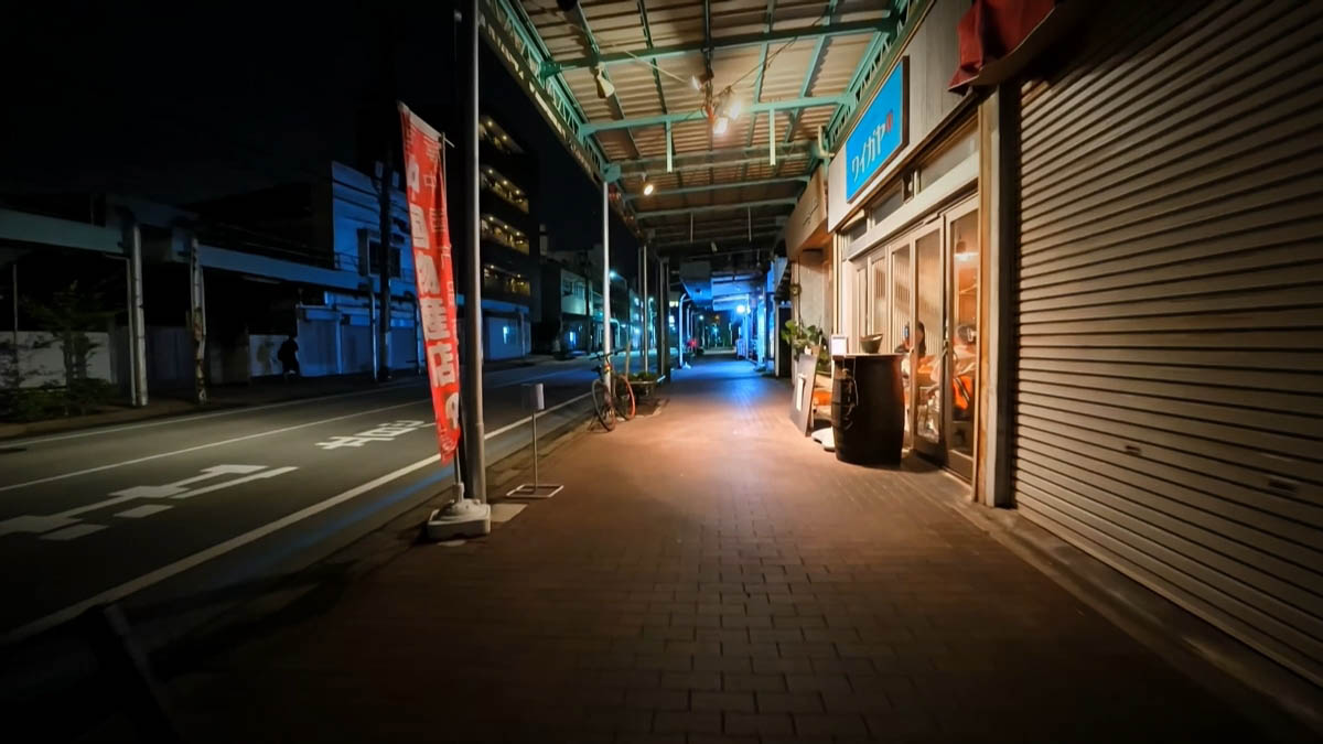 Waigaya Waigaya bar with a blue sign and wooden barrel table; red banner for a Chinese goods store