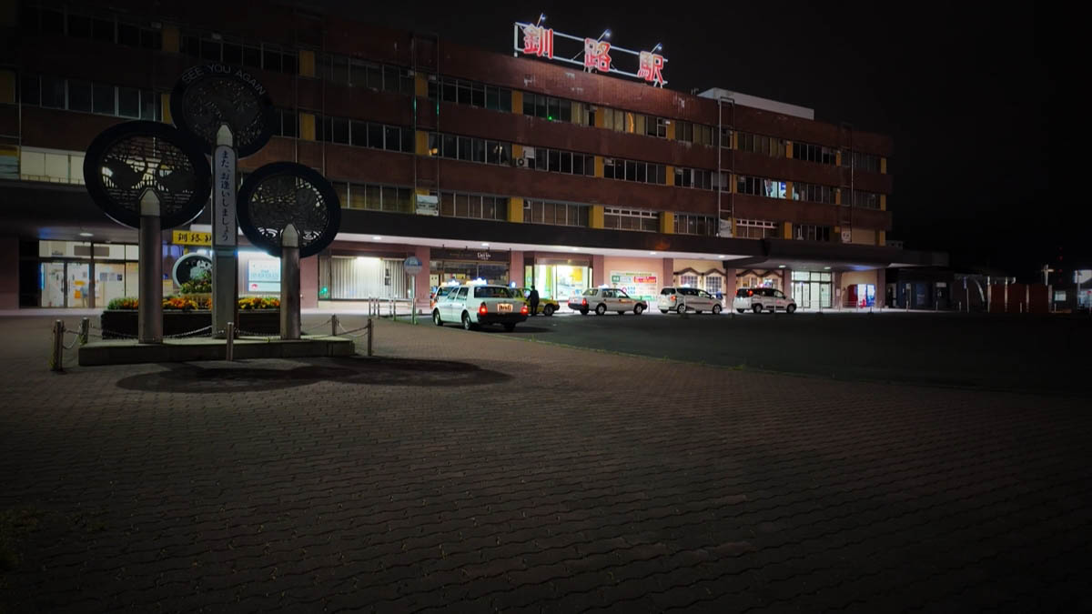 Red neon Kushiro Station roof sign and taxi stand; “See you again” monument in the foreground