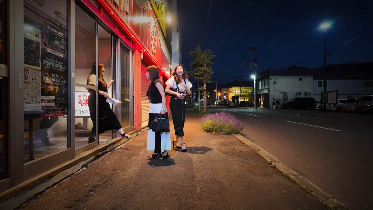 赤い電飾の店先で話す三人