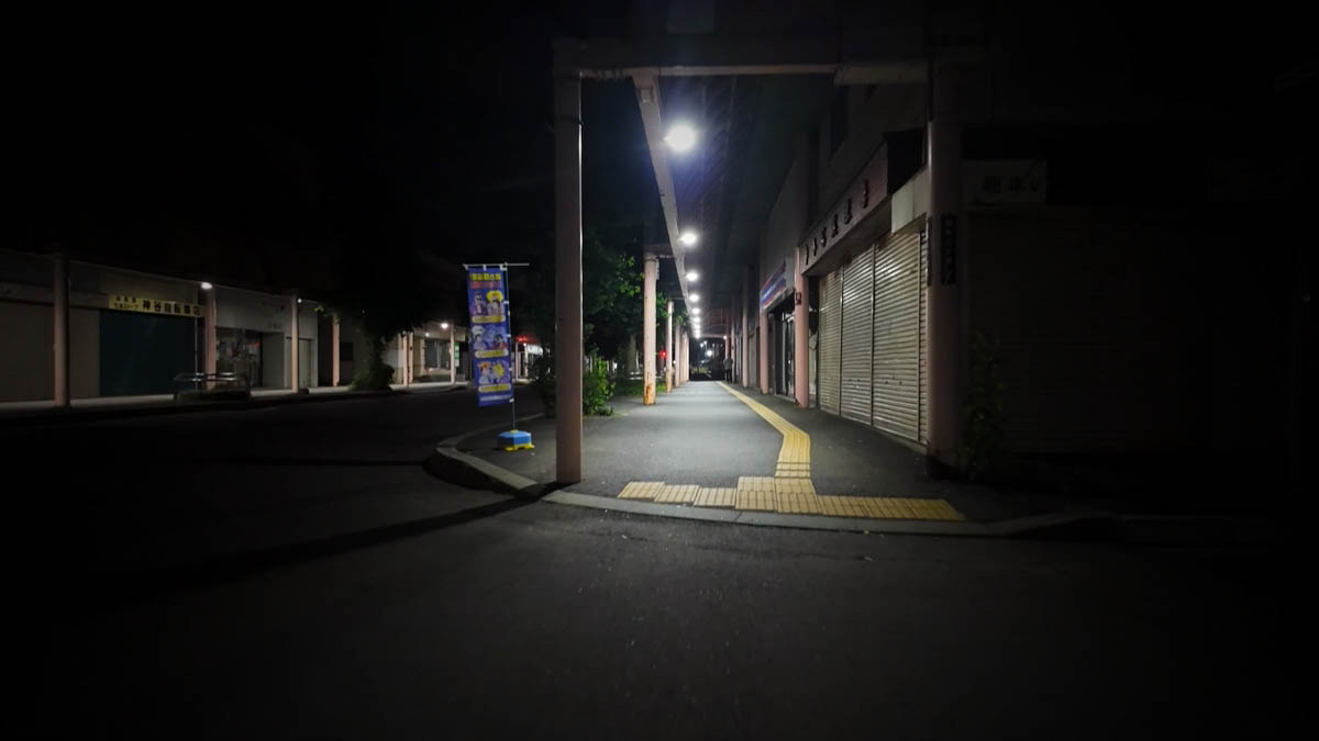 Empty arcade, shutters down, tactile paving vanishing into the dark