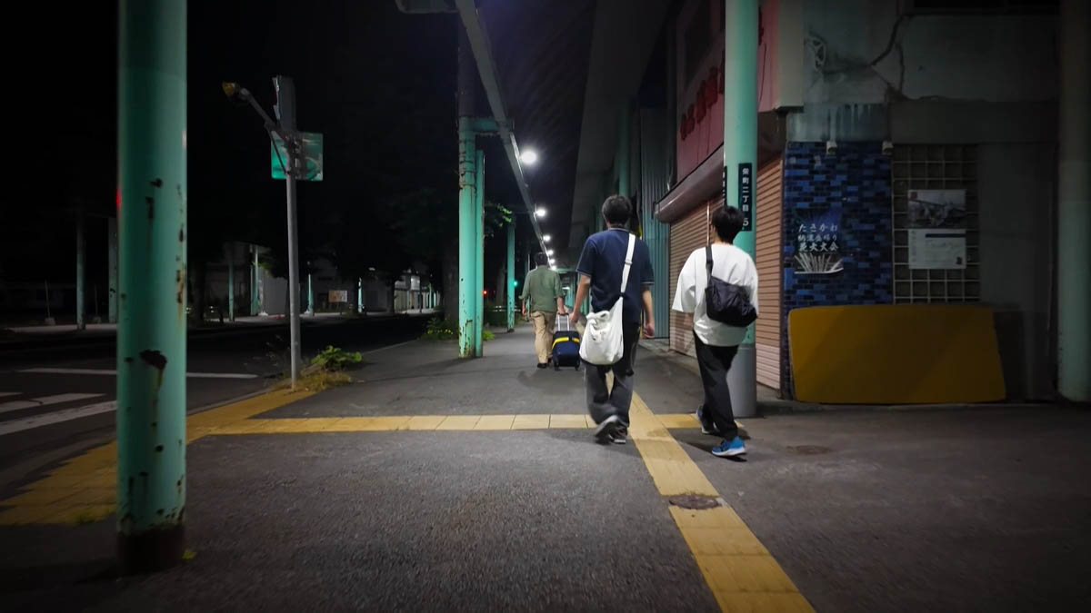 Three men ahead on the sidewalk, one pulling a suitcase