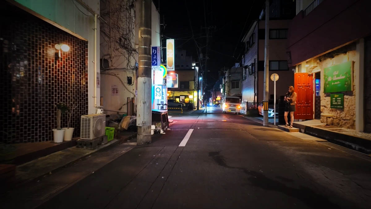 飲み屋の路地 細い路地。赤いドアの前に立つ女性